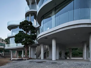 A modern building with curved glass walls and a tree in front, surrounded by potted plants and a contemporary urban atmosphere