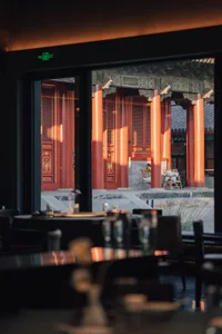 A traditional Asian restaurant with red columns and walls, featuring dining tables with various objects and a person in the background