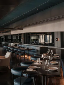 Modern restaurant interior with black and grey tones, multiple tables, chairs, and wine glasses, creating a sophisticated atmosphere