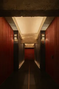 Dimly lit industrial-style hallway with red walls, wooden floors, and two doors on either side