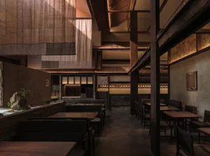 A modern restaurant interior with wooden floors and walls, featuring dining tables and chairs in a warm and inviting atmosphere