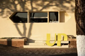 A modern coffee shop with a yellow sign reading Up, a white exterior, and outdoor seating with cups and bottles scattered around