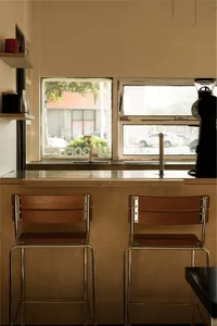 Warm kitchen with two wooden chairs near a window, two sinks, and natural light