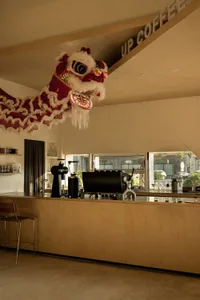 A vibrant Asian restaurant interior with a wooden dragon head, chairs, a dining table, and various cups and bottles, evoking a sense of cultural heritage and tradition