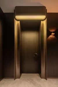 A long wooden hallway with a door on the right side, featuring a gold handle, in a quiet and empty atmosphere