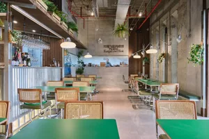 Empty restaurant interior with green tables and chairs, white and red walls, and potted plants, creating a clean and organized atmosphere