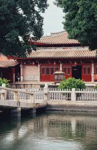 A tranquil Asian-style building with red walls and white trim, surrounded by courtyards and multiple rooms, with people walking around the area
