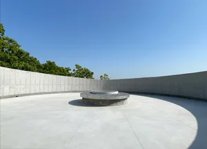 A serene outdoor space with a circular stone structure surrounded by a cement wall and trees in the background
