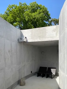極簡風客廳與餐廳空間，擁有清水混凝土牆、兩把椅子、一張長椅，以及引入自然光的窗戶