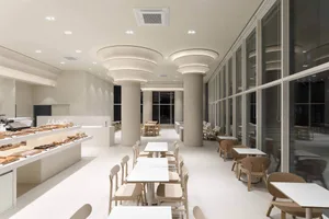 Clean and modern restaurant interior with white walls, beige chairs, and tables, featuring a minimalist dining area with several tables and chairs