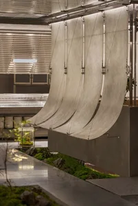 Modern industrial space with a large metal sculpture hanging from the ceiling, made of metal rods resembling a sail