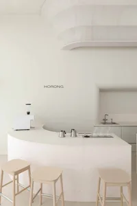 Modern kitchen with white walls and countertops, featuring two sinks, cups, a bowl, and three chairs around a dining table