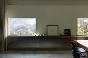 Empty living room with a large window, two chairs, a dining table, and a vase, with sunlight entering the space