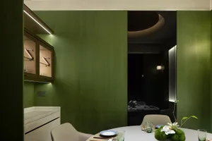 A modern kitchen and dining area with green walls, a dining table, chairs, and various decorative items