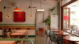Dining area with multiple tables, chairs, and potted plants, surrounded by modern tiled walls