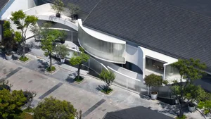 A modern building with a large glass wall and concrete facade, featuring potted plants and a sophisticated atmosphere