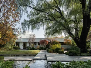 A serene architectural scene featuring a white building surrounded by trees, potted plants, and a central bench, with a mix of photo and rendered elements