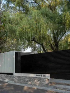 A black exterior wall and white interior wall of an Asian-style house with a stone wall and wooden fence, surrounded by trees