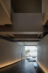 An interior space with a large window overlooking a body of water, featuring modern architecture with concrete and glass elements