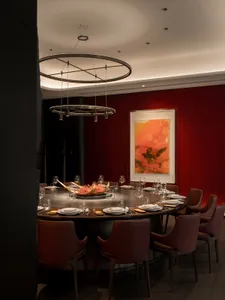 Elegant dining area with a round table, red wall, wine glasses, and bottles, creating a sophisticated atmosphere