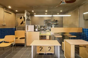 Modern coffee shop interior with a counter, sinks, refrigerator, and seating areas, featuring a clean and functional design