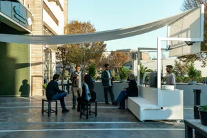 An outdoor cafe with a large white canopy, potted plants, and people sitting on benches and chairs