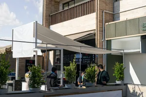 An outdoor dining area with potted plants, chairs, and people socializing in a lively setting
