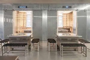 A modern kitchen and dining area with two dining tables, stainless steel walls, chairs, and well-lit space