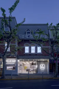 A modern Asian restaurant with white walls, gray floors, and natural light from a large window, featuring chairs and dining tables in a clean and minimalist space