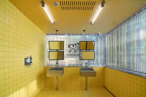 Bathroom with two sinks on yellow tiled walls, metal sinks, and natural light from a window