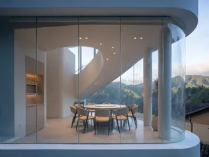 Open living area with glass walls, natural light, chairs, dining table, and a potted plant