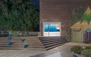 A modern building with a large window and concrete exterior, featuring two chairs outside in a nighttime setting