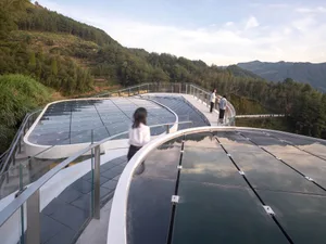 A modern building with a glass roof, featuring a combination of glass and metal elements, with people walking around on the upper level