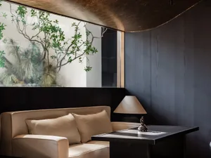 Cozy living space with a white couch, wooden chair, and a potted plant, featuring a dining table in the background