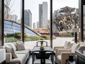A well-lit indoor living area with a large window offering a city view, featuring two couches, a dining table, chairs, and decorative accents