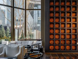 A modern dining space with a lit tile wall, comfortable seating, and potted plants, conveying a stylish and inviting atmosphere