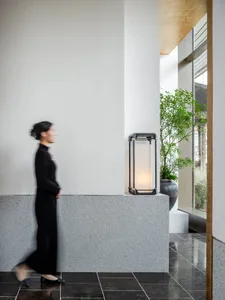 A woman walks down an office hallway with two potted plants and a suitcase on the floor