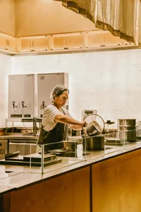 一位女性在工業風廚房中於檯面上準備食物，周圍環繞著碗盤與廚具，在注重細節的專業環境中