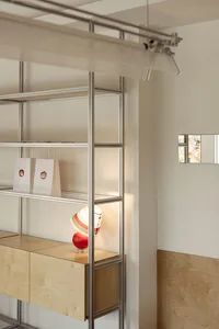 A metal bookshelf with two bags and books on a white wall, creating a calm and organized atmosphere