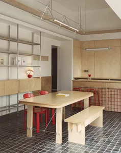 A warm and inviting kitchen and dining area with a wooden table, two red chairs, a smaller dining table, a sink, and a refrigerator, surrounded by books and exuding a cozy atmosphere