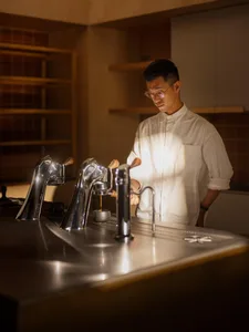 A man prepares coffee in a kitchen with three sinks and various kitchen equipment