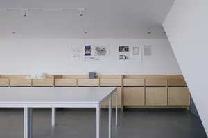 Professional office space with white walls, wooden cabinets, and a table surrounded by chairs, featuring several displayed design drawings