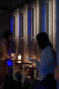 Two women sitting at a wooden bar with cups and a bottle, in a relaxed social setting