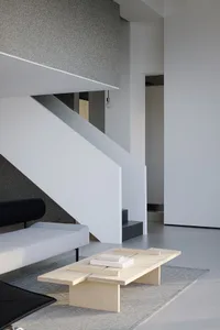Cozy modern living area with a couch, staircase, and bookshelf, featuring white walls and grey carpeting