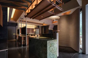 A restaurant dining area with tables, chairs, potted plants, wood, and stone walls, and various lighting fixtures