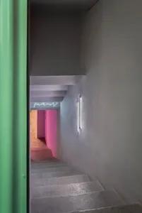 A colorful hallway with a staircase, painted walls in pink, green, and purple, and lights on both sides