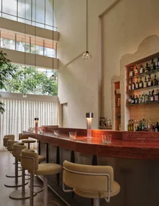 A bar area with a wooden counter, stools, bottles, and wine glasses, creating an inviting atmosphere with nearby chairs and tables