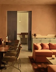A modern living space with a large couch, dining table, chairs, kitchen area, refrigerator, and sink, featuring a warm and inviting atmosphere