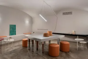 現代咖啡廳，白色餐桌搭配橙色凳子，周圍環繞座椅，並有窗戶自然光線灑入
