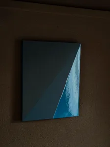 A framed piece of abstract artwork with blue and white elements mounted on a wall in a room